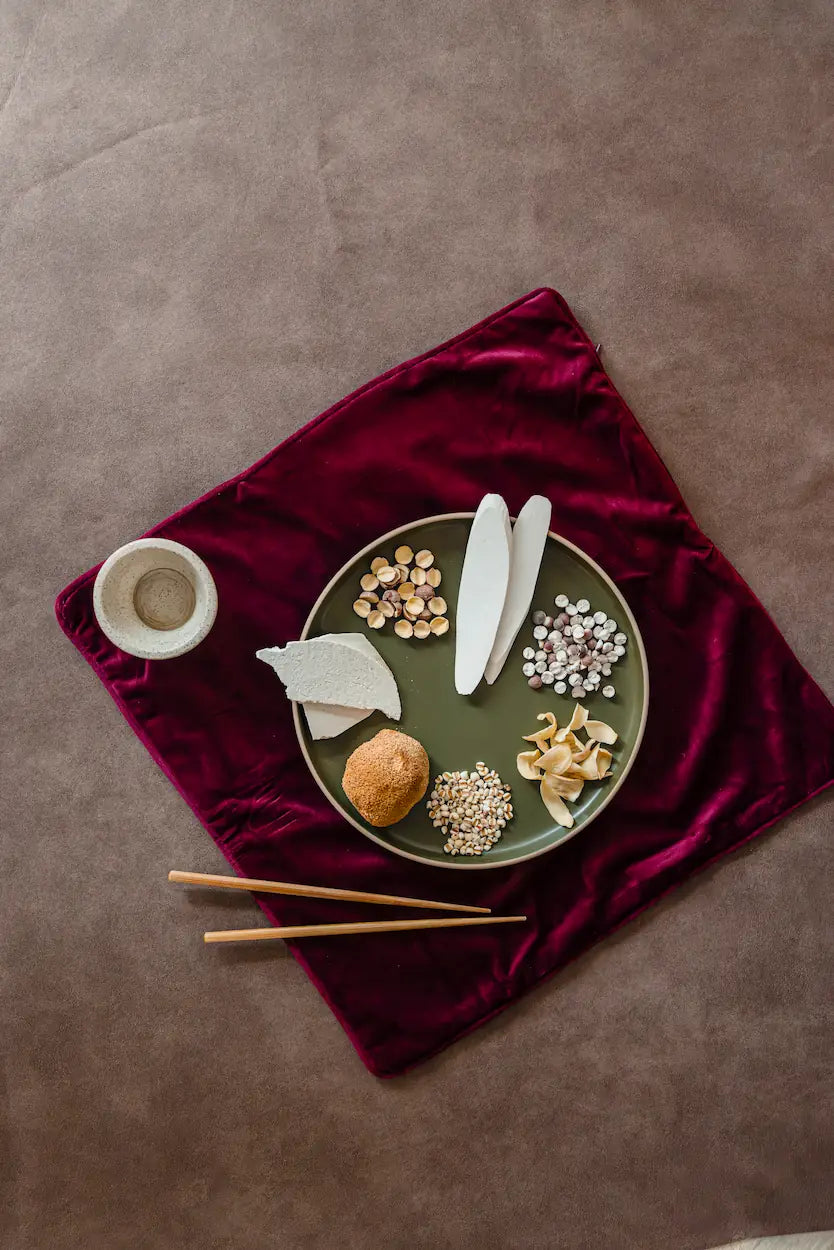 棕色背景下红丝绒布上的绿色盘子，盛放中式月子草本