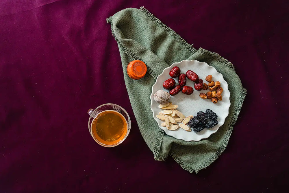 Dried herbs and a cup of tea on a green cloth against a dark background