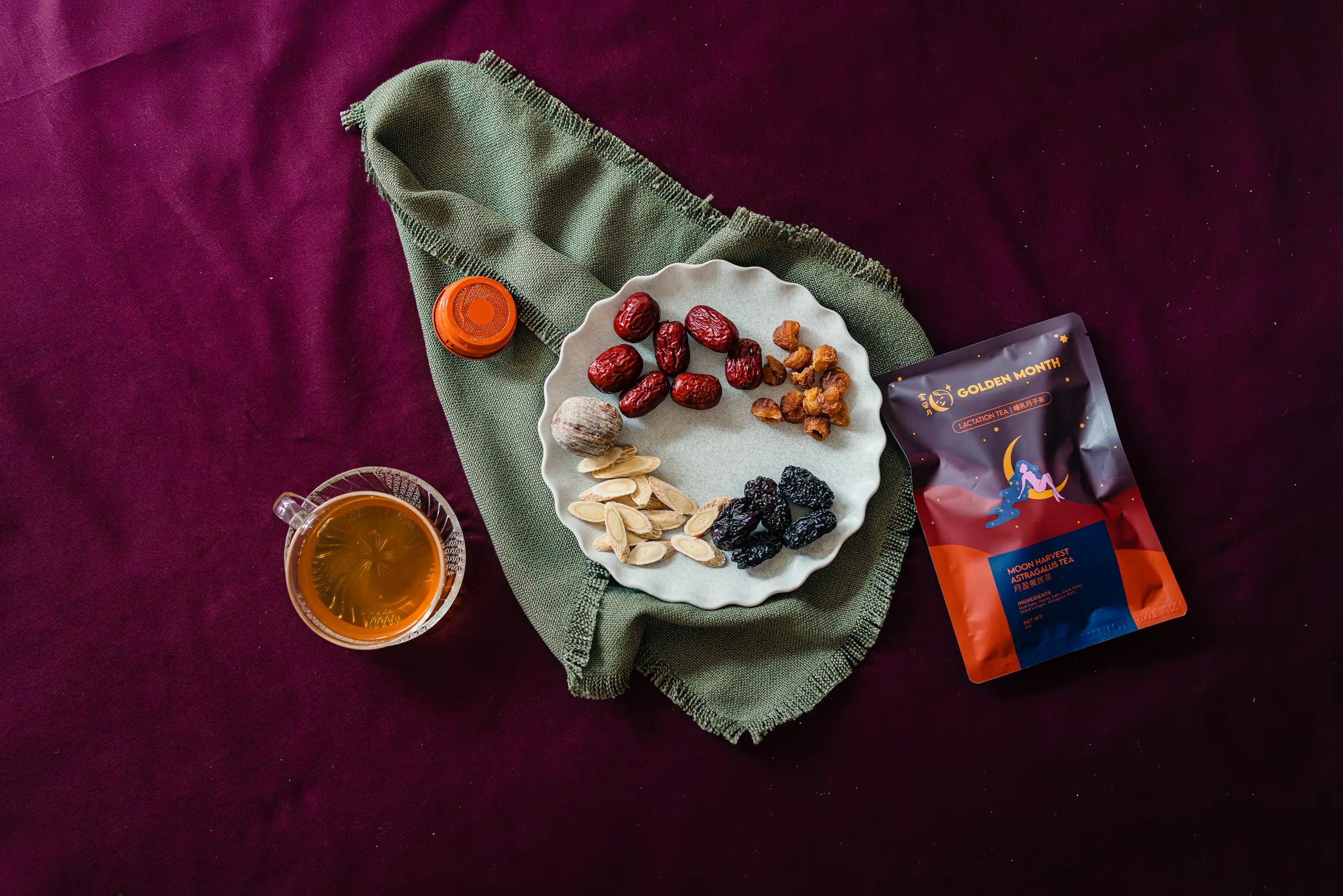 Dried fruits and chinese herbs on a plate with a cup of tea and a package on a purple fabric background