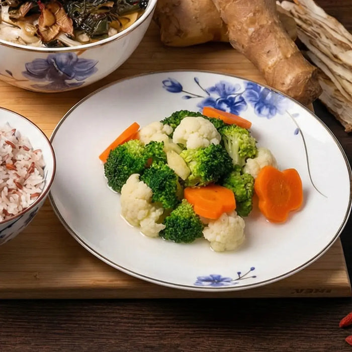 Plate of vegetables including broccoli and carrots on a wooden table with bowls of rice and another dish.